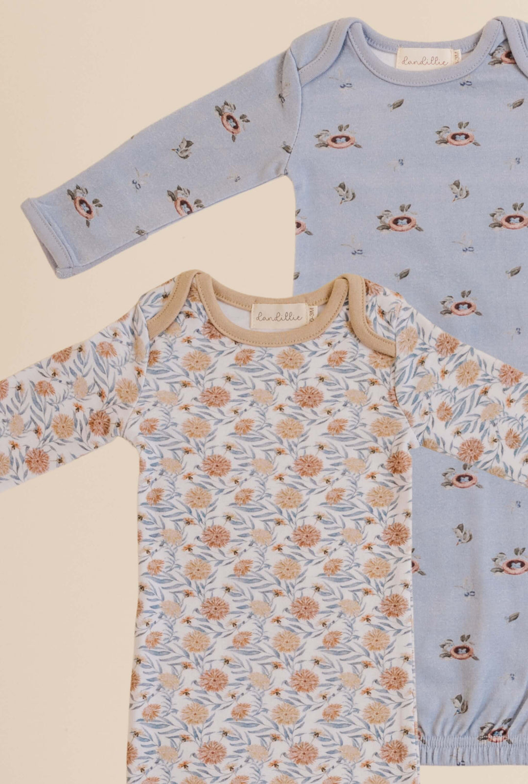 Two baby bodysuits with floral and bird prints on a beige background